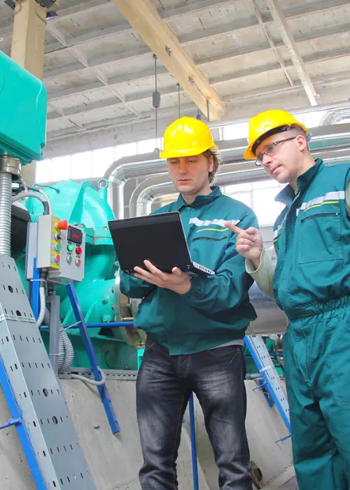 ingeniería acústica en planta industrial, revisando datos en laptop junto a maquinaria para diagnóstico y acústica ingeniería aplicada al control de ruido y mejoras operacionales.