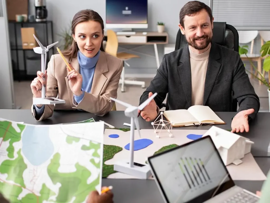 Equipo de consultoría ambiental analiza mapas y maquetas de aerogeneradores en oficina, con consultor ambiental y asesora ambiental planificando evaluación y medidas para proyectos del SEIA.